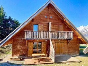 A wooden cabin with a balcony, large wooden doors, and a small table outside.