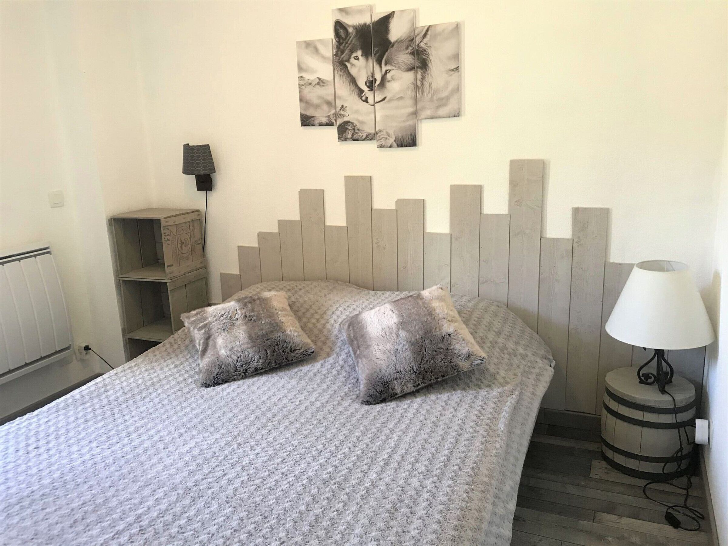 A bedroom with a bed, two pillows, a headboard, a lamp, a radiator, and a shelf.