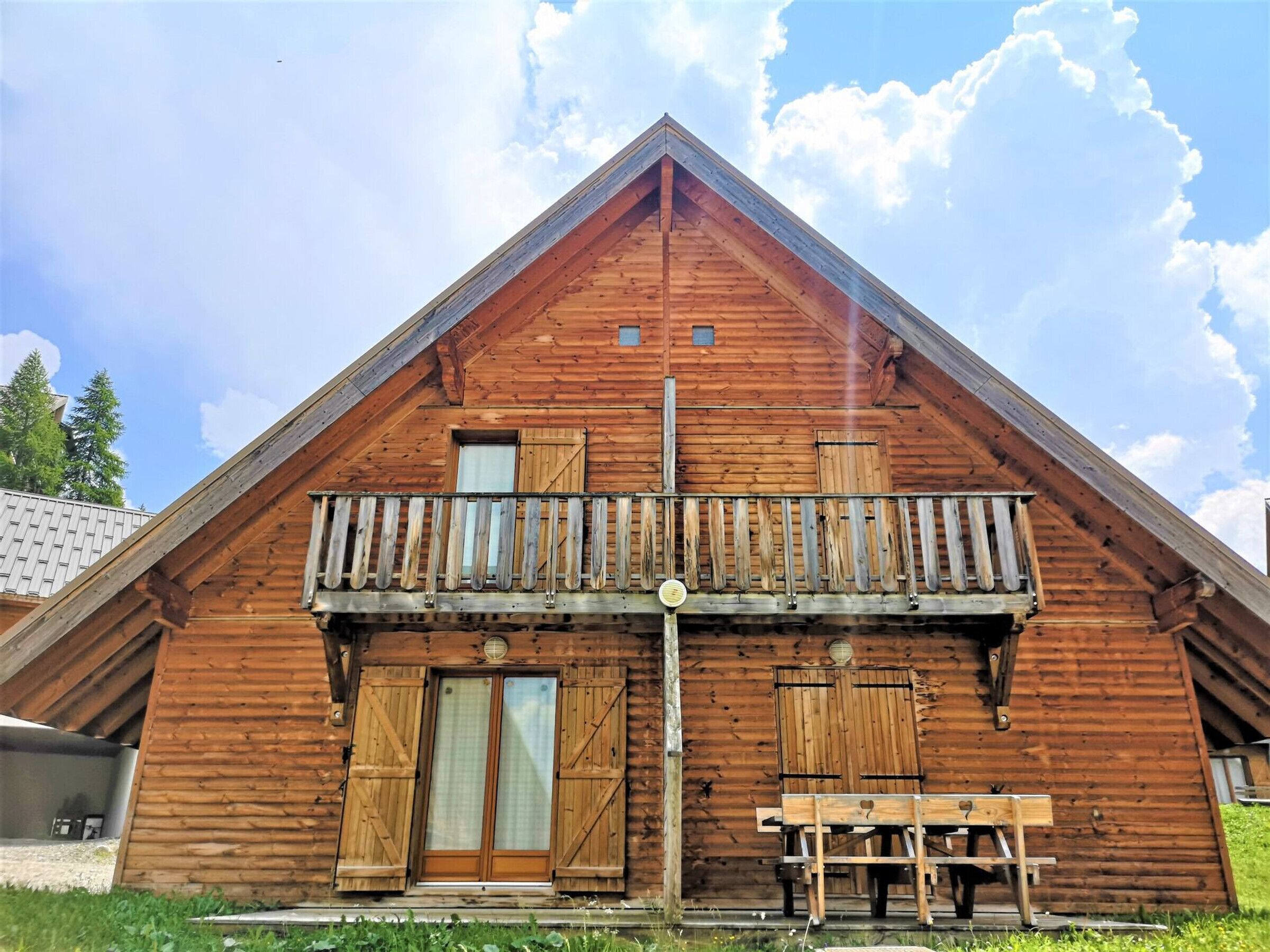 A wooden cabin with a balcony, a door, and a bench.