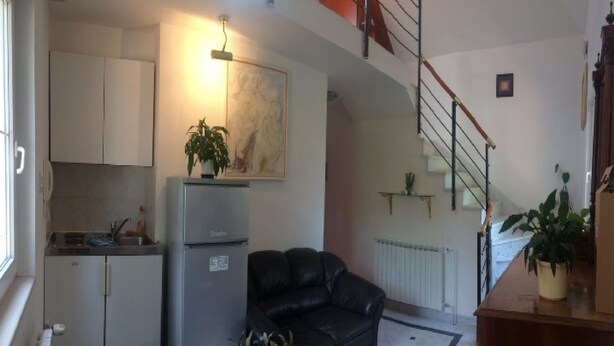 A compact living space with a kitchenette, a black leather sofa, a dining table, and a staircase leading to an upper level. - Apartment Simba (Supetar)