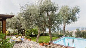Area piscina con patio in pietra, mobili da esterno e piante in vaso.