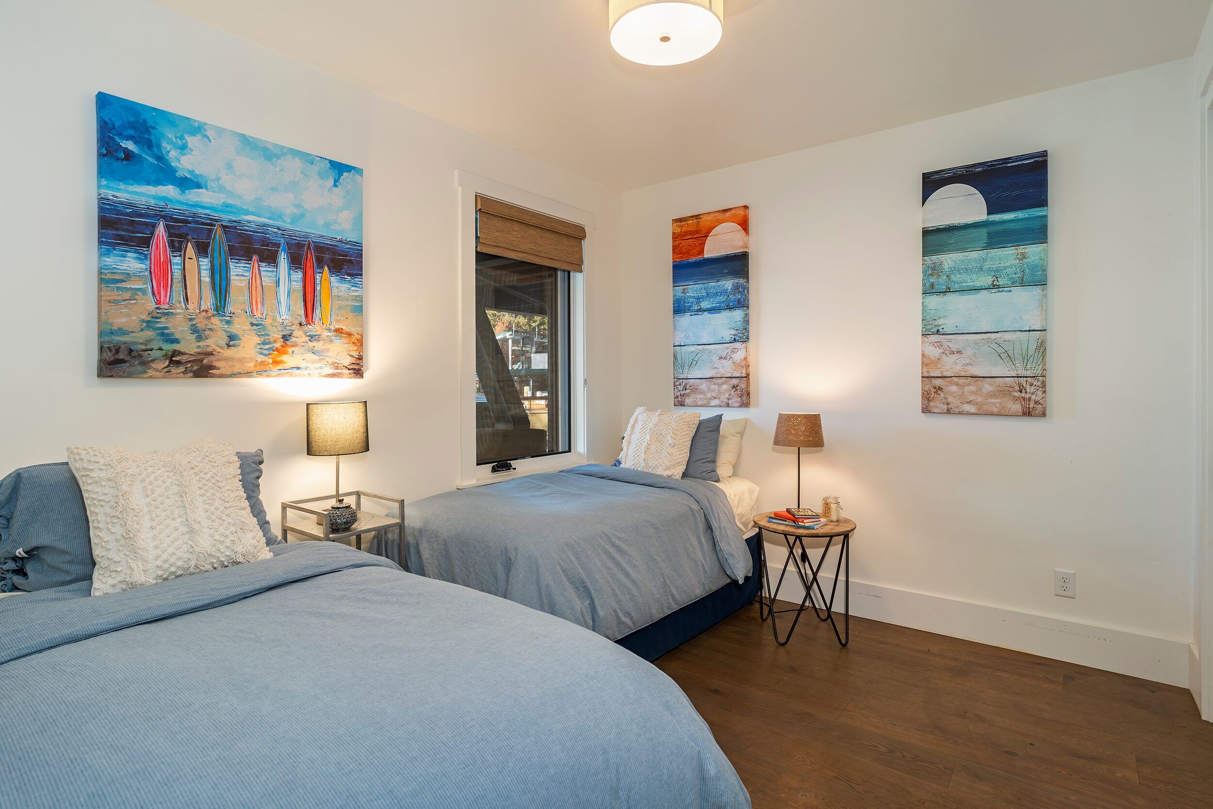 A bedroom with two beds, a window with a view, and artwork on the walls.