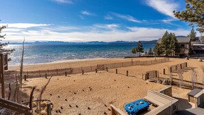 A beach with a wooden fence, a sandy area, and a view of the sea and mountains. - Tahoe Beachfront Retreat 2 -  Tahoe Lakefront Condo with Amazing Views, Minutes to Trails and Golf (Kings Beach)