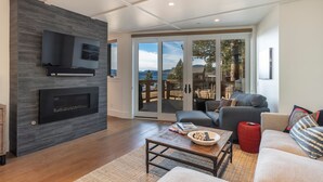 A modern living room with a fireplace, a flat-screen TV, and a large sliding glass door leading to a deck. - Tahoe Beachfront Retreat 2 -  Tahoe Lakefront Condo with Amazing Views, Minutes to Trails and Golf (Kings Beach)