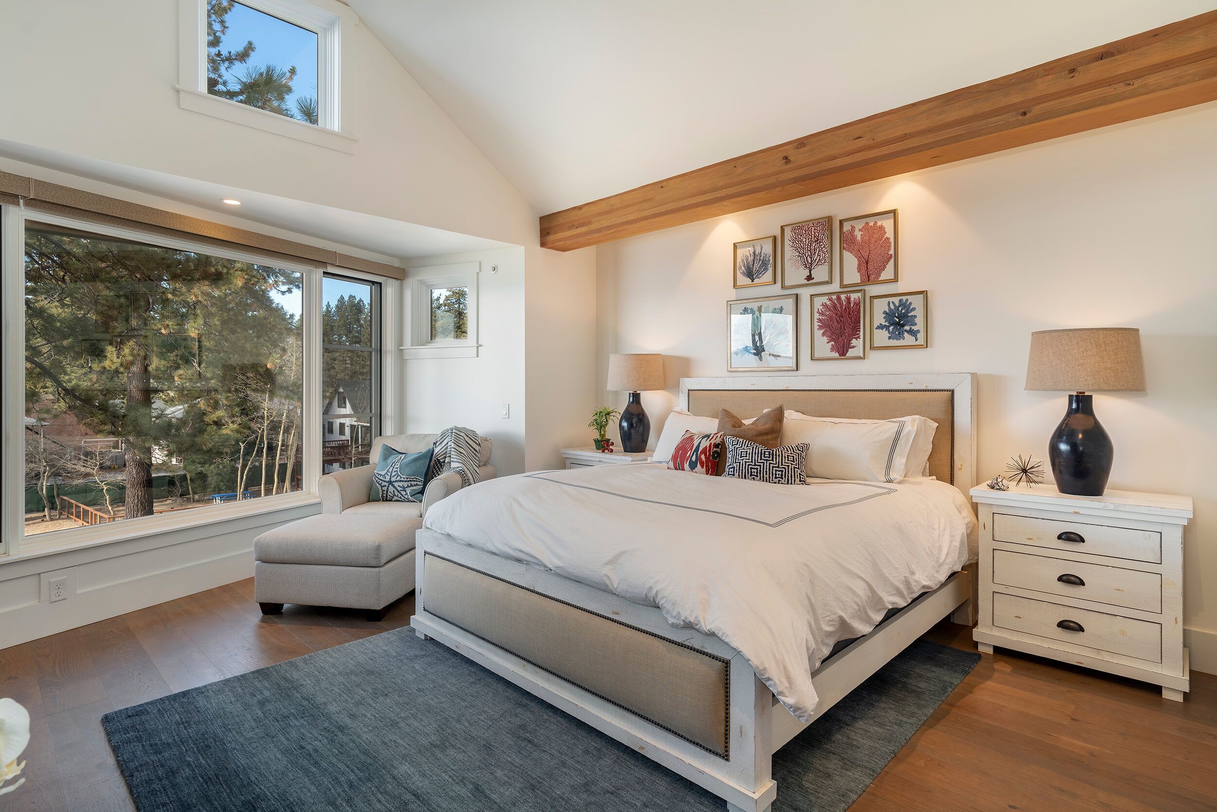 A bedroom with a large window, a bed with a headboard, bedside tables, and wall art.