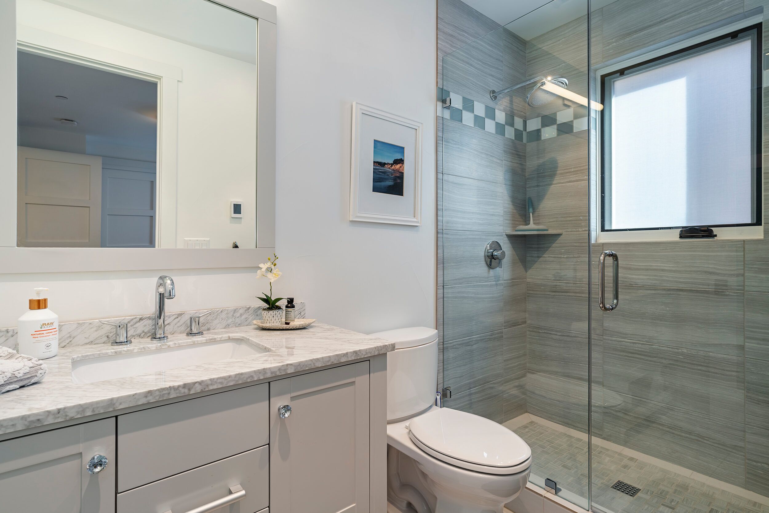 A modern bathroom with a marble sink, a toilet, and a glass shower enclosure.