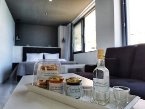 A hotel room with a bed, a sofa, and a table with a tray containing jars of Sunrise Luxury Sea Side Apartments.