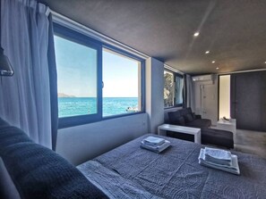 A modern bedroom with a large window, a bed, a sofa, and a small table.