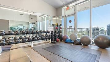 Un gimnasio con equipo de ejercicio, un espejo y grandes ventanales con vistas a la ciudad.