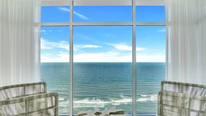 A room with a large window overlooking the ocean, two wicker chairs, and a stone sculpture. - Daytona Grande Oceanfront Resort (Daytona Beach)