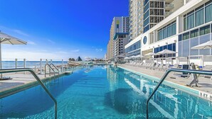A swimming pool with clear blue water, surrounded by modern buildings and a view of the ocean. - Daytona Grande Oceanfront Resort (Daytona Beach)