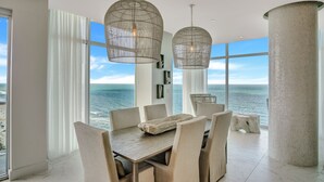 A dining area with a large table and chairs, large windows with ocean views, and hanging pendant lights. - Daytona Grande Oceanfront Resort (Daytona Beach)