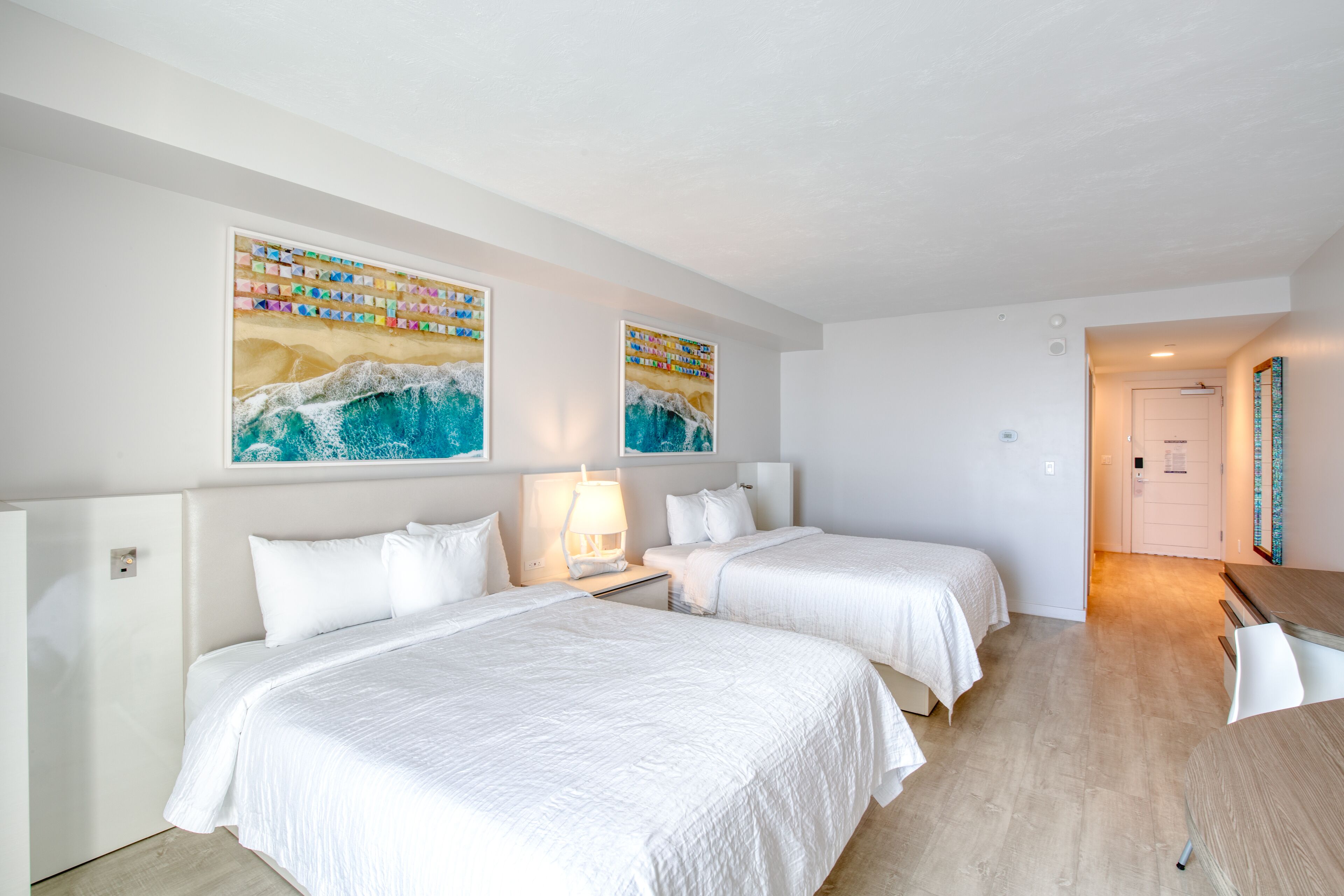A hotel room with two beds, a wooden floor, and artwork on the wall.