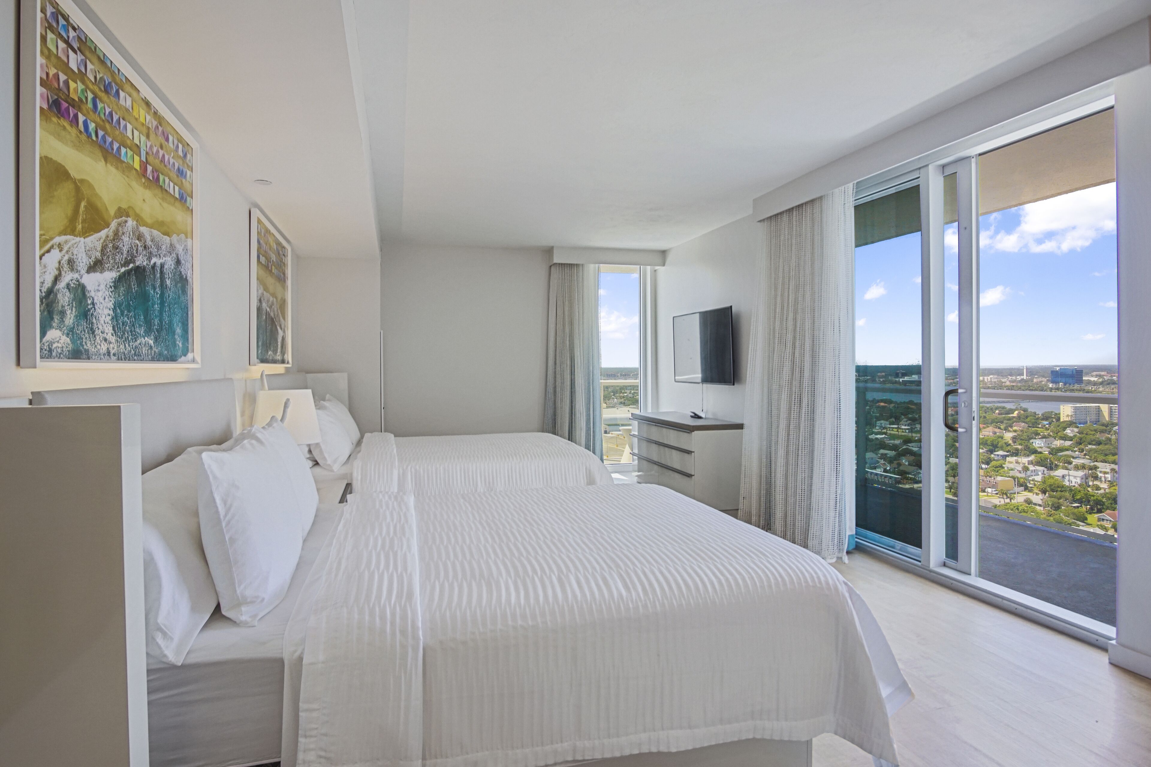 A modern hotel room with a large bed, a TV, and a balcony with a city view.