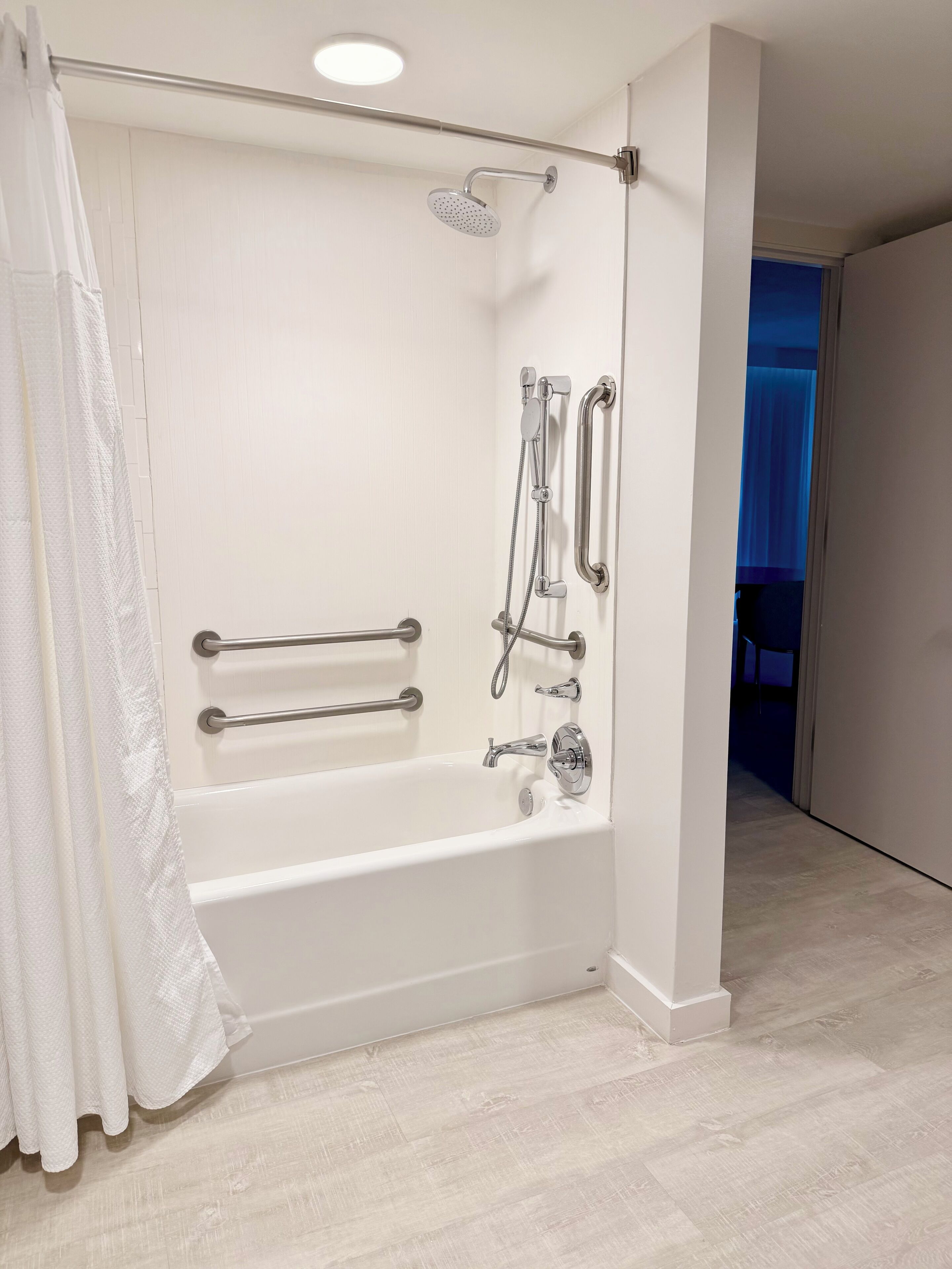 A modern bathroom with a white bathtub, grab bars, a handheld showerhead, and a walk-in shower.