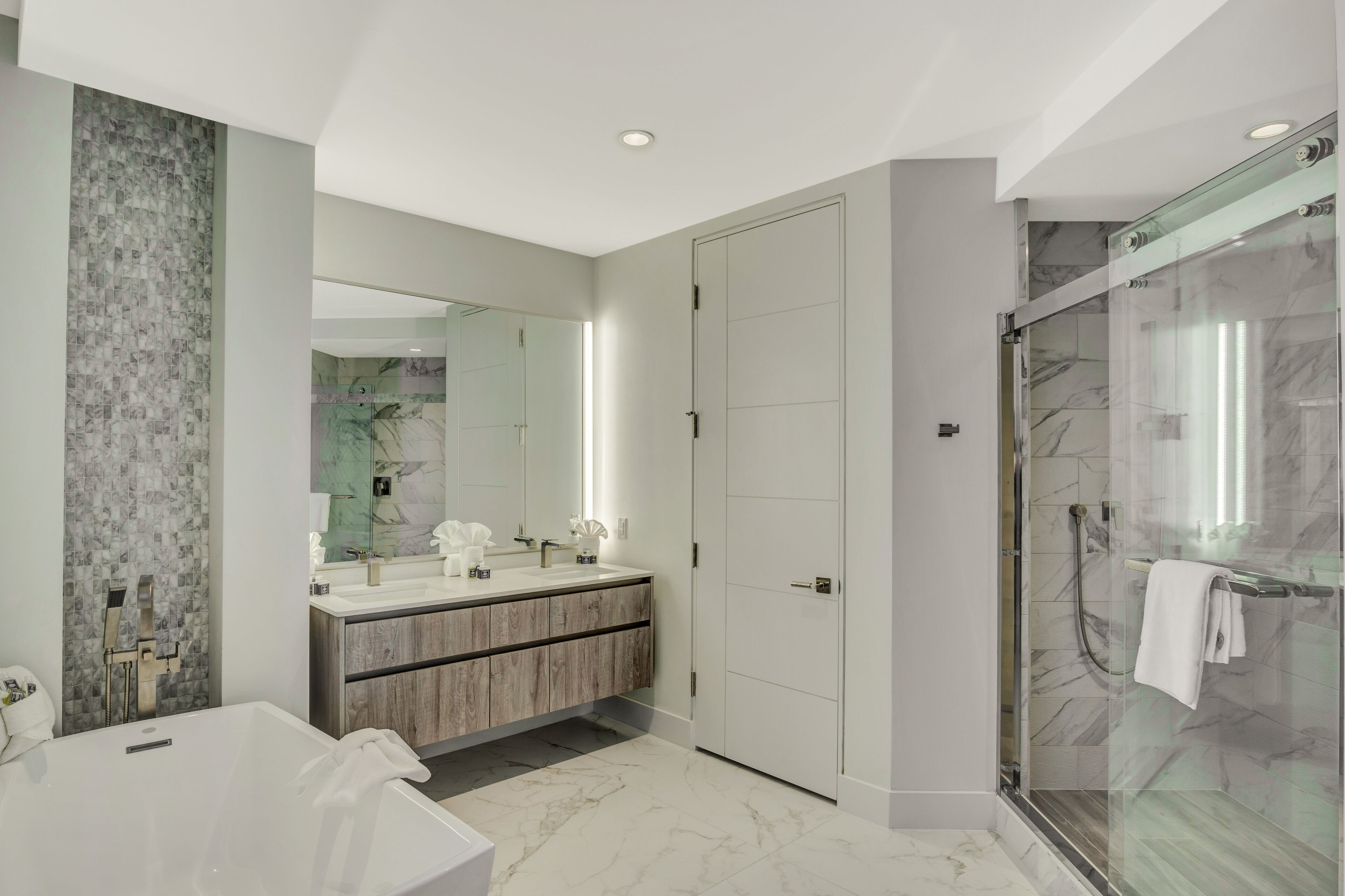 A modern bathroom with a large mirror, a bathtub, a shower area, and a vanity with a marble countertop.