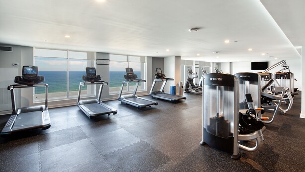 A gym with treadmills, elliptical machines, and weight equipment, large windows with a view of the ocean. - Daytona Grande Oceanfront Resort (Daytona Beach)