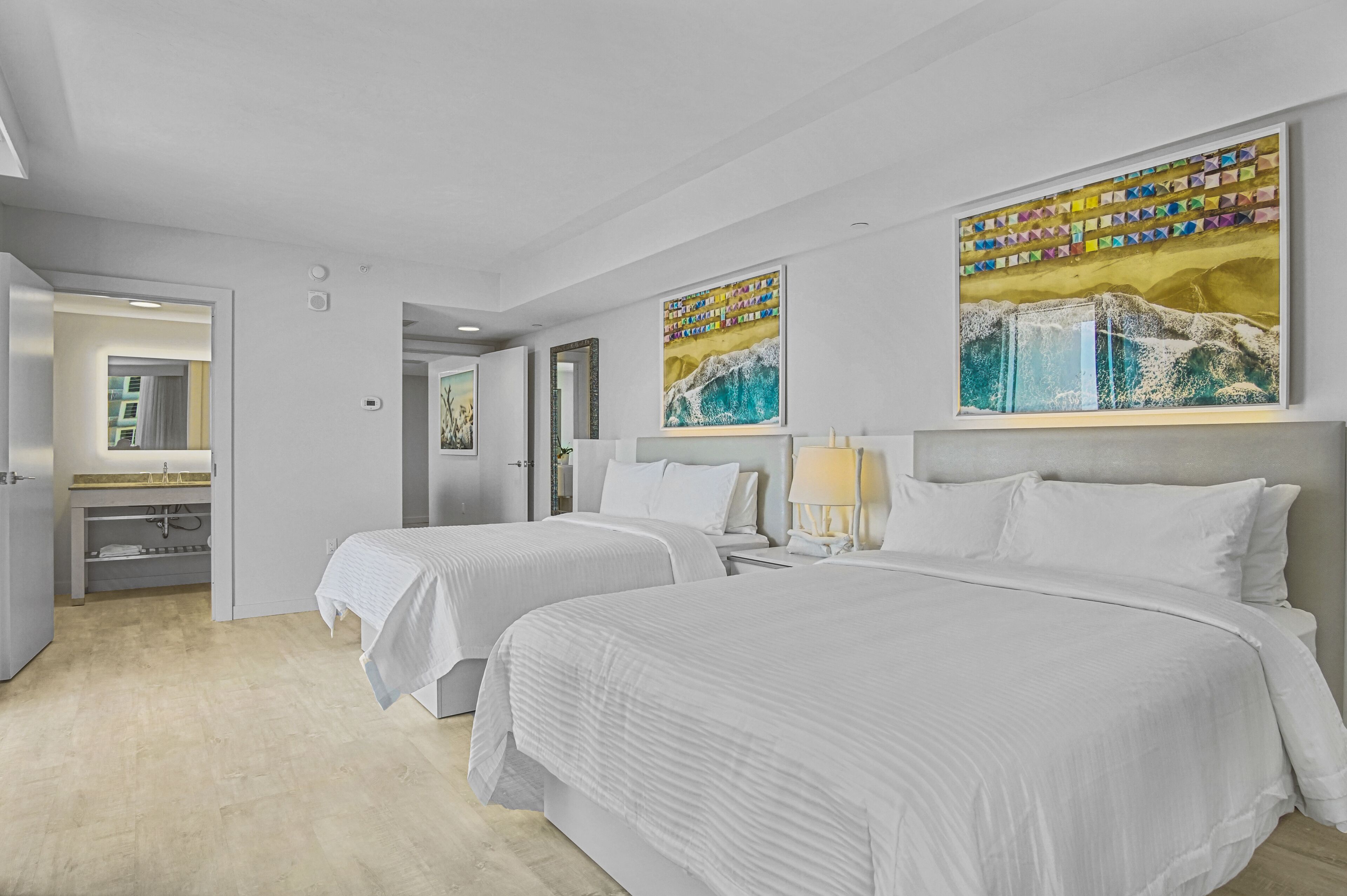 Ein Hotelzimmer mit zwei Betten, einem Badezimmer und Bildern an den Wänden.