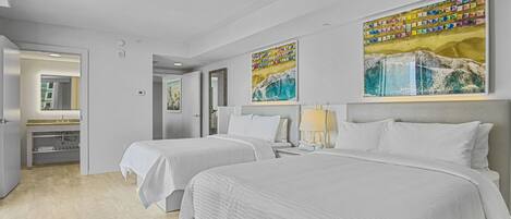 A hotel room with two beds, a bathroom, and artwork on the walls.