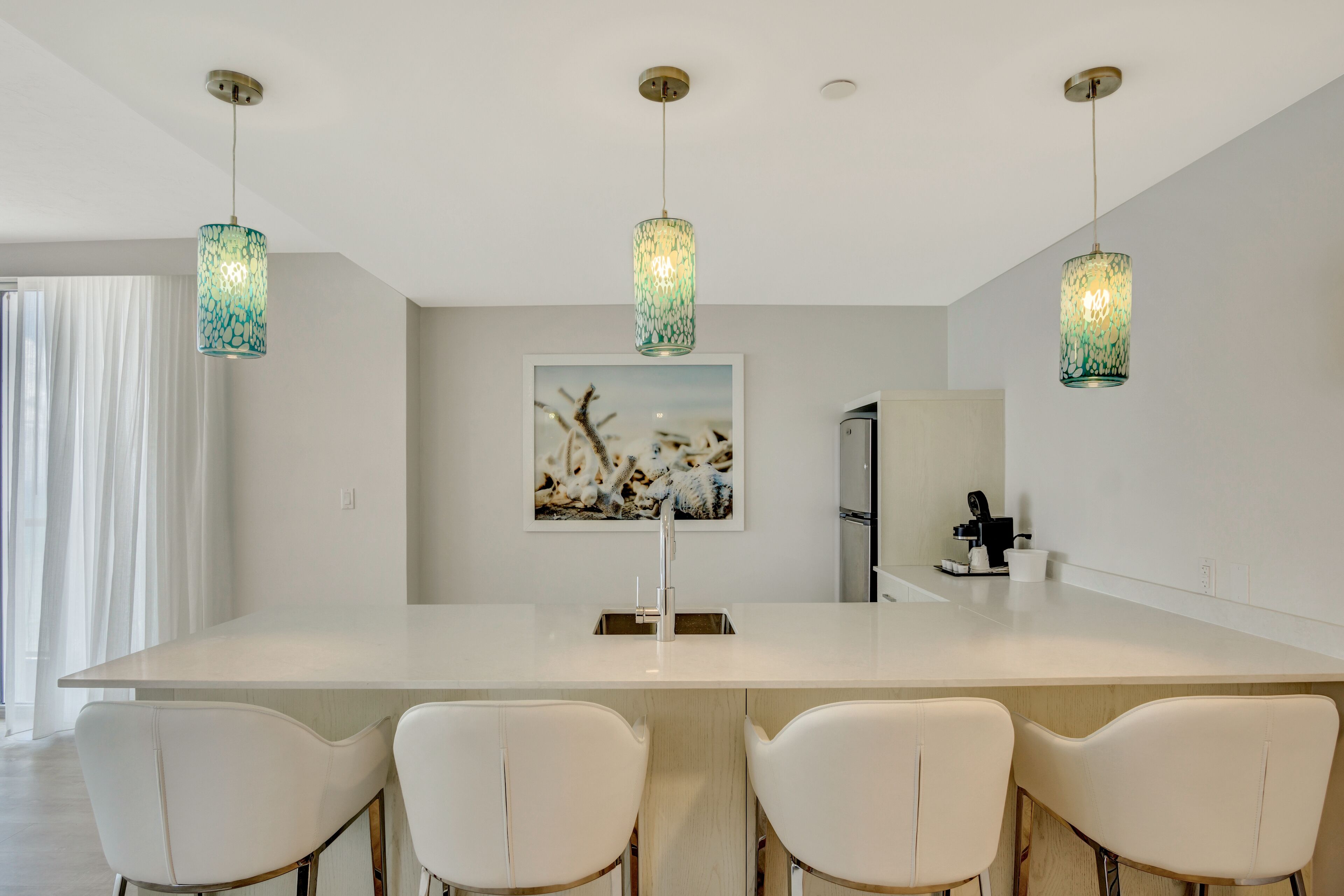 Una cocina moderna con una isla grande, sillas blancas e iluminación colgante.