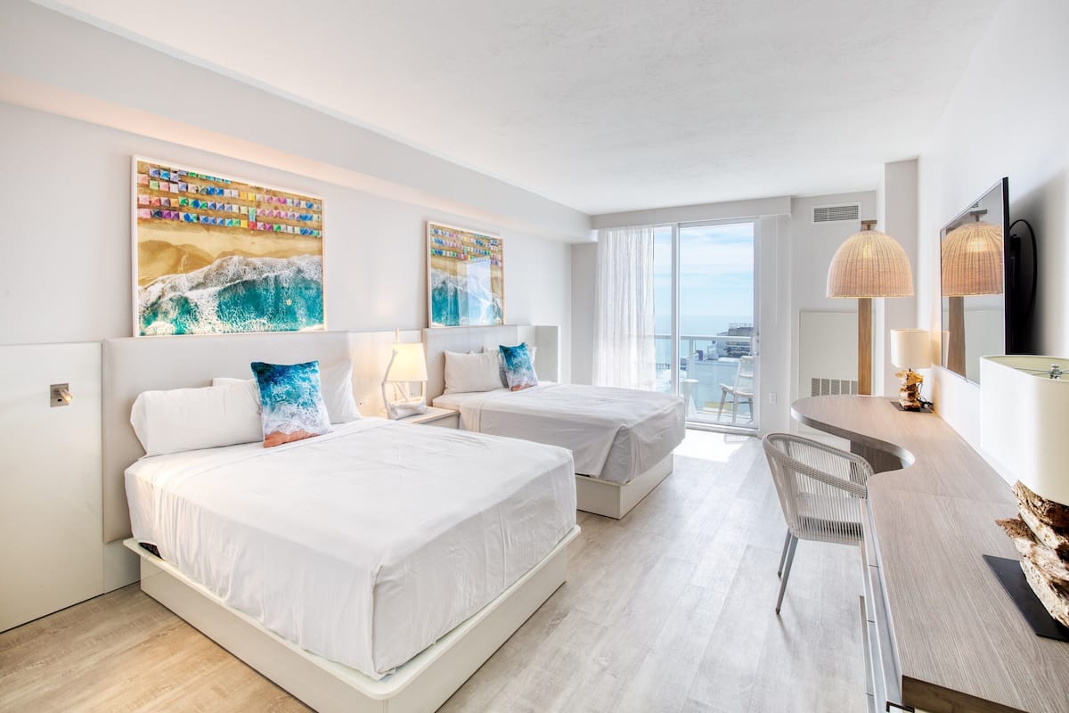 Ein modernes Hotelzimmer mit zwei Betten, einem Schreibtisch und einem Balkon mit Aussicht.