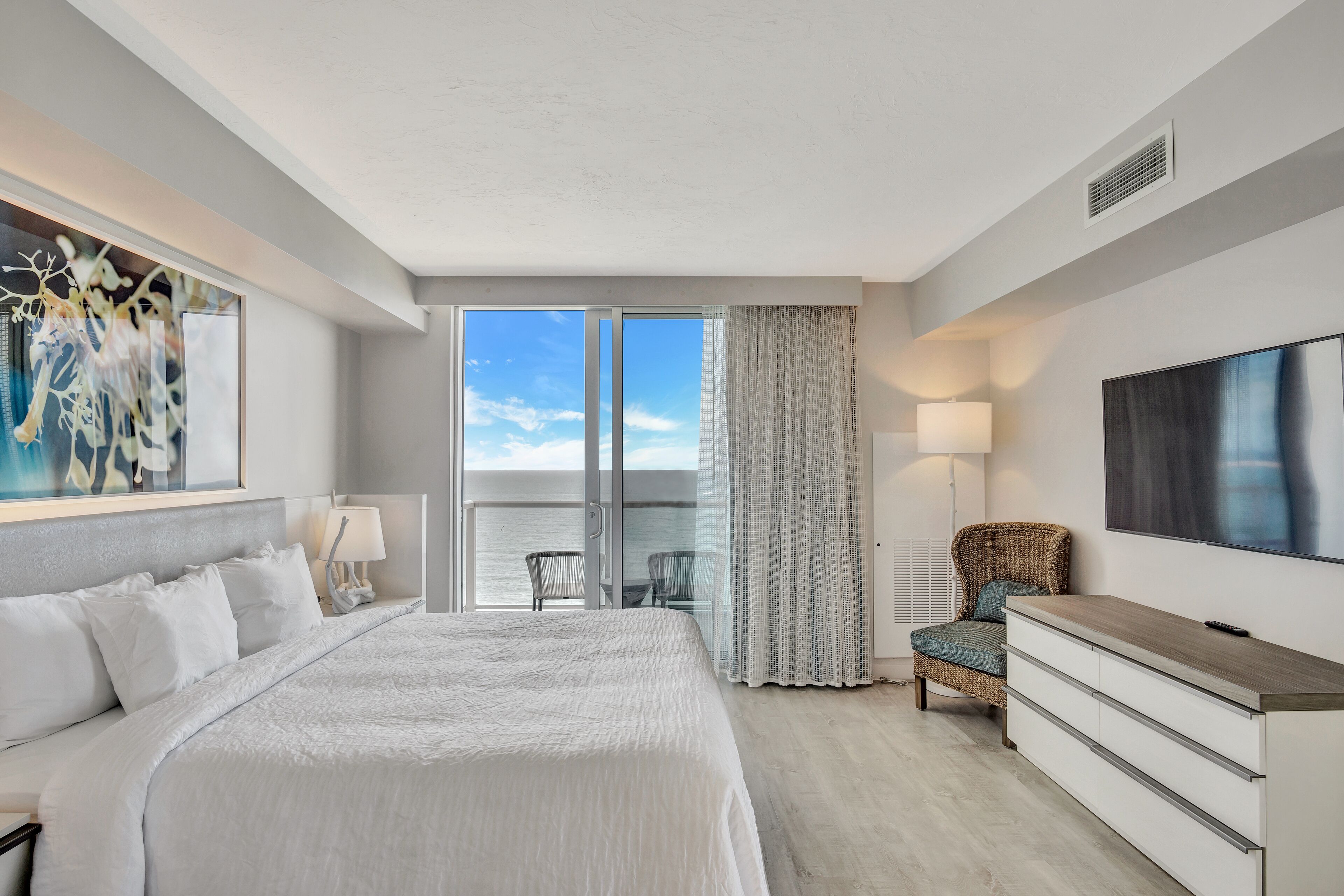 Habitación de hotel con una cama grande, televisor, cómoda, una silla y balcón con vistas.