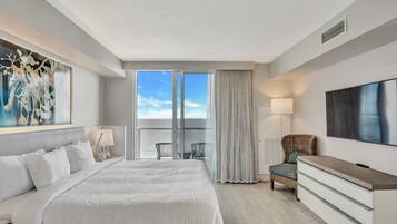 A hotel room with a large bed, a TV, a dresser, a chair, and a balcony with a view.