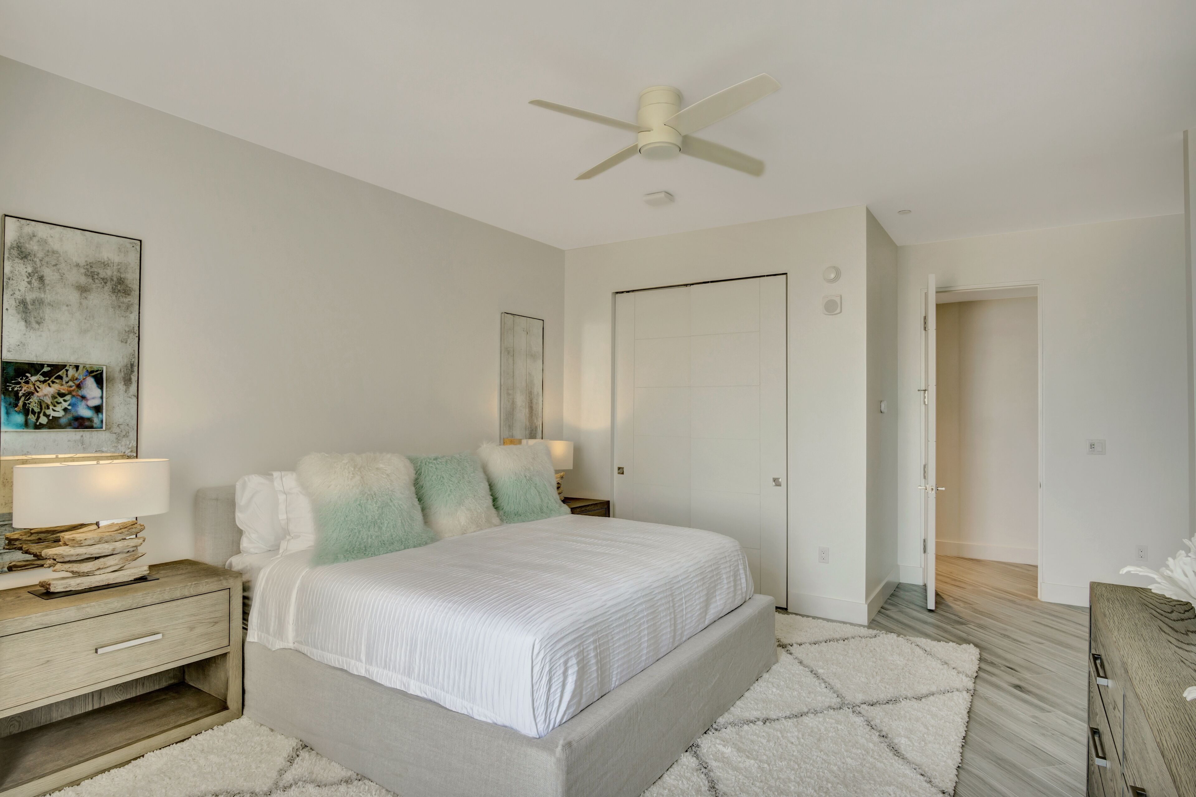 A bedroom with a bed, nightstands, a ceiling fan, and a door leading to another room.