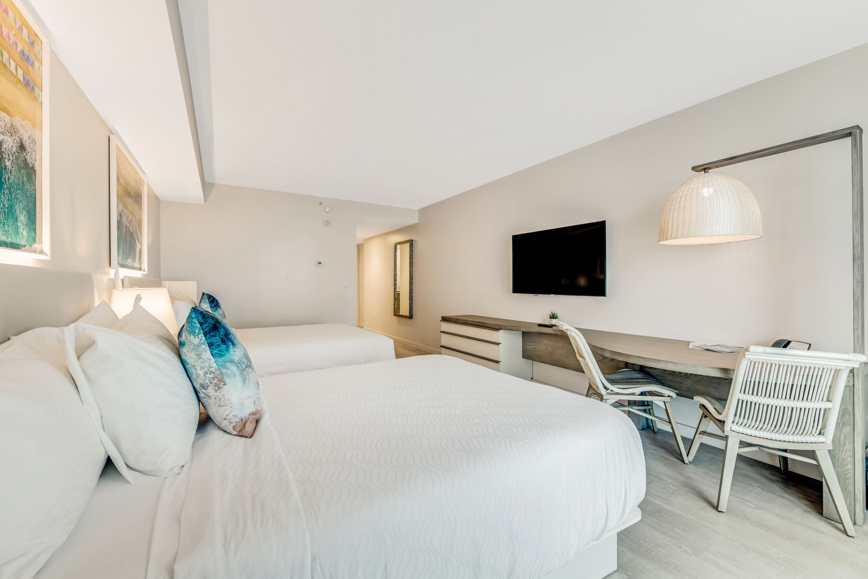 A modern hotel room with two beds, a desk, a chair, a TV, and a large window.