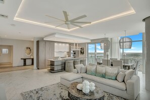 A modern living room with a large sectional sofa, a coffee table, and a view of the city.