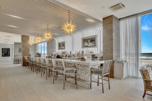 A modern bar area with a long counter, multiple bar stools, and pendant lighting.