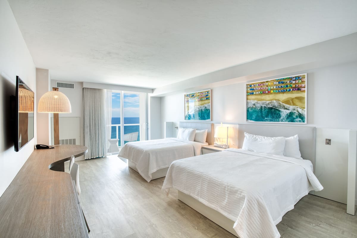 Ein Hotelzimmer mit zwei Betten, einem Schreibtisch, einem Fernseher und Bildern an den Wänden.