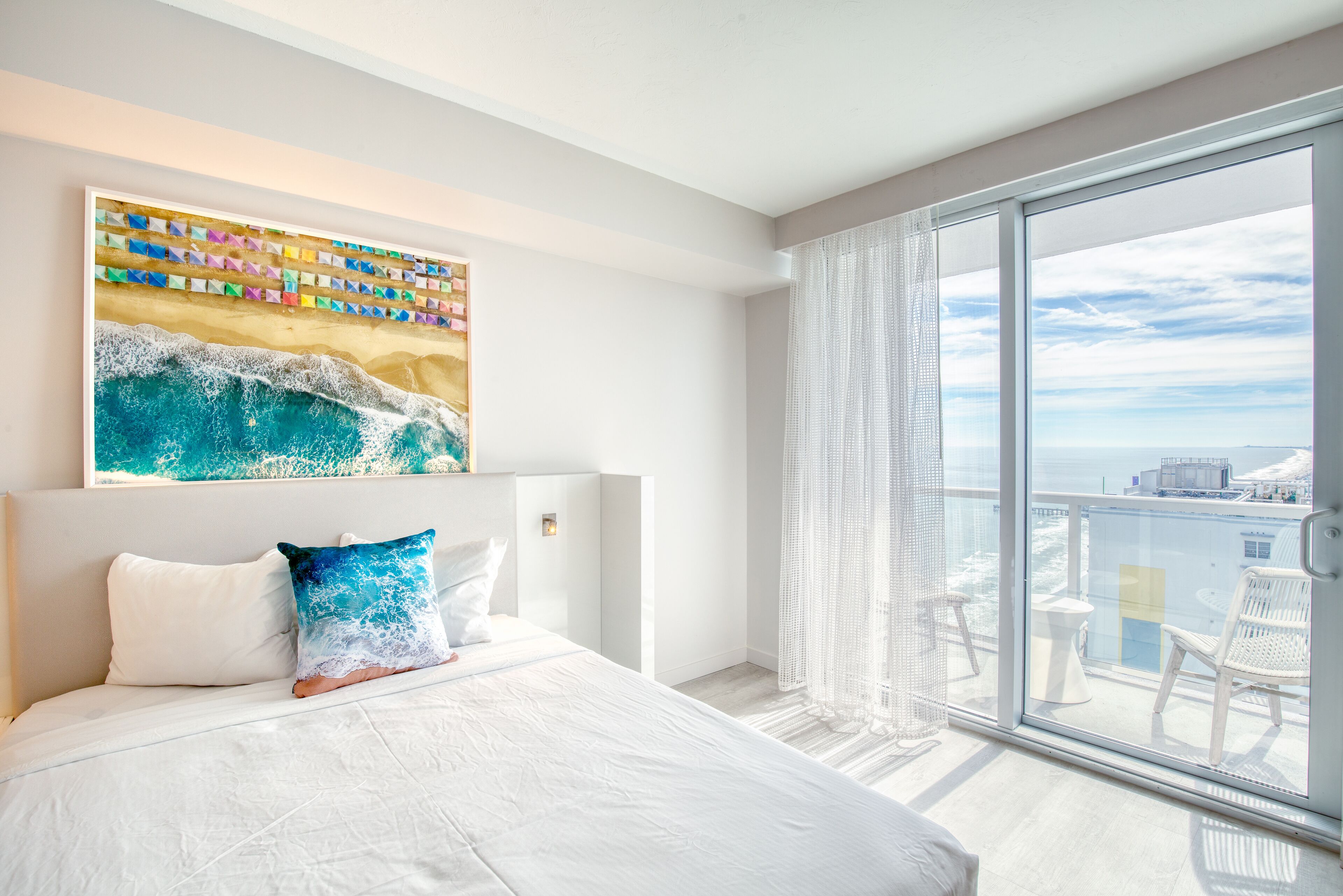 A modern hotel room with a large bed, a colorful artwork above the bed, and a balcony with a view of the city.