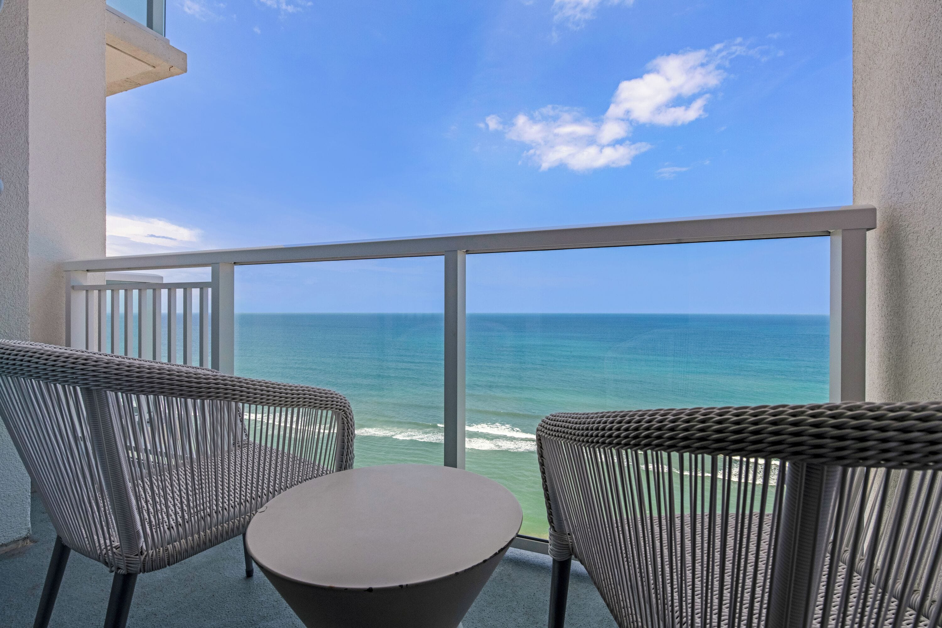 A balcony with wicker chairs and a table, overlooking a clear blue ocean.
