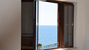 Ein Zimmer mit großem Fenster und Meerblick, inklusive Balkon mit Geländer und weißer Wand.