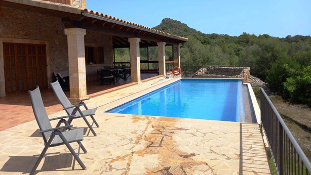 Zona de piscina con sillones reclinables, un porche cubierto y una terraza de piedra.