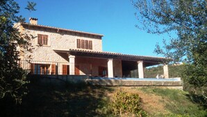 Una casa de piedra de dos plantas con un porche cubierto y una piscina.