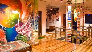 A vibrant interior with a large wall mural, wooden flooring, and a staircase with colorful flag decorations. -  Skyard Hostel Rishikesh (Laxman Jhula) (Yamkeshwar)