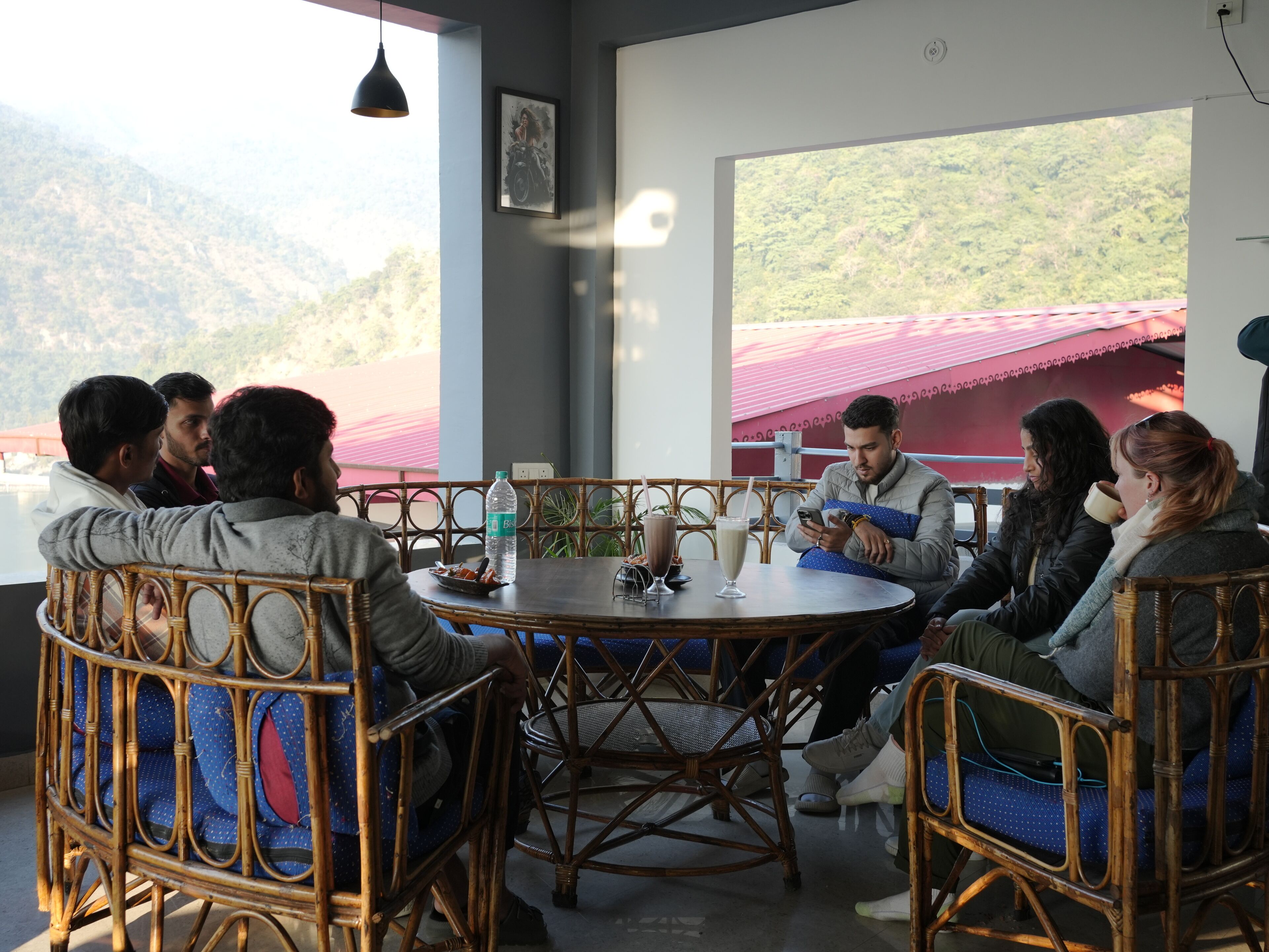 A group of people seated around a round table in a room with large windows overlooking a mountainous landscape.