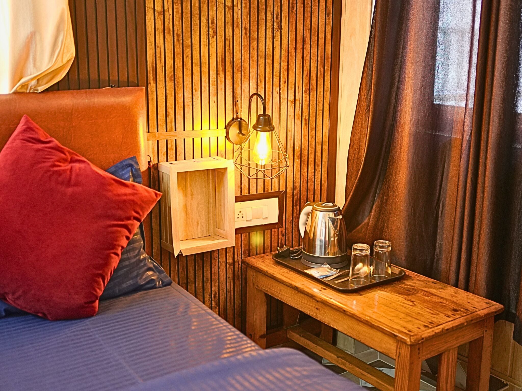 A cozy room with a bed, a wooden nightstand, a kettle, and a tray with glasses.