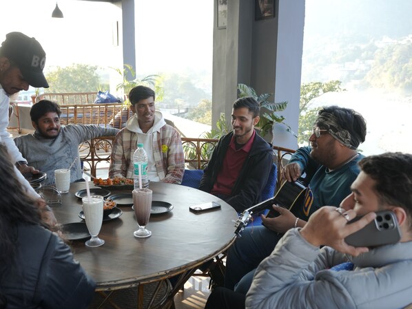 Un grupo de personas sentadas alrededor de una mesa redonda en un café con vistas a las colinas.