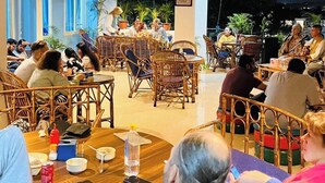 A dining area at Skyard Hostels with wicker furniture and a central table with food and drinks. -  Skyard Hostel Rishikesh (Laxman Jhula) (Yamkeshwar)