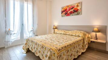 A bedroom with a bed, curtains, a painting, and bedside lamps.