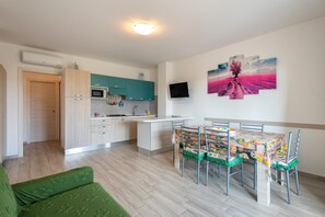 Une cuisine moderne avec des meubles de couleur turquoise, un coin repas avec une table et des chaises, et un téléviseur fixé au mur.