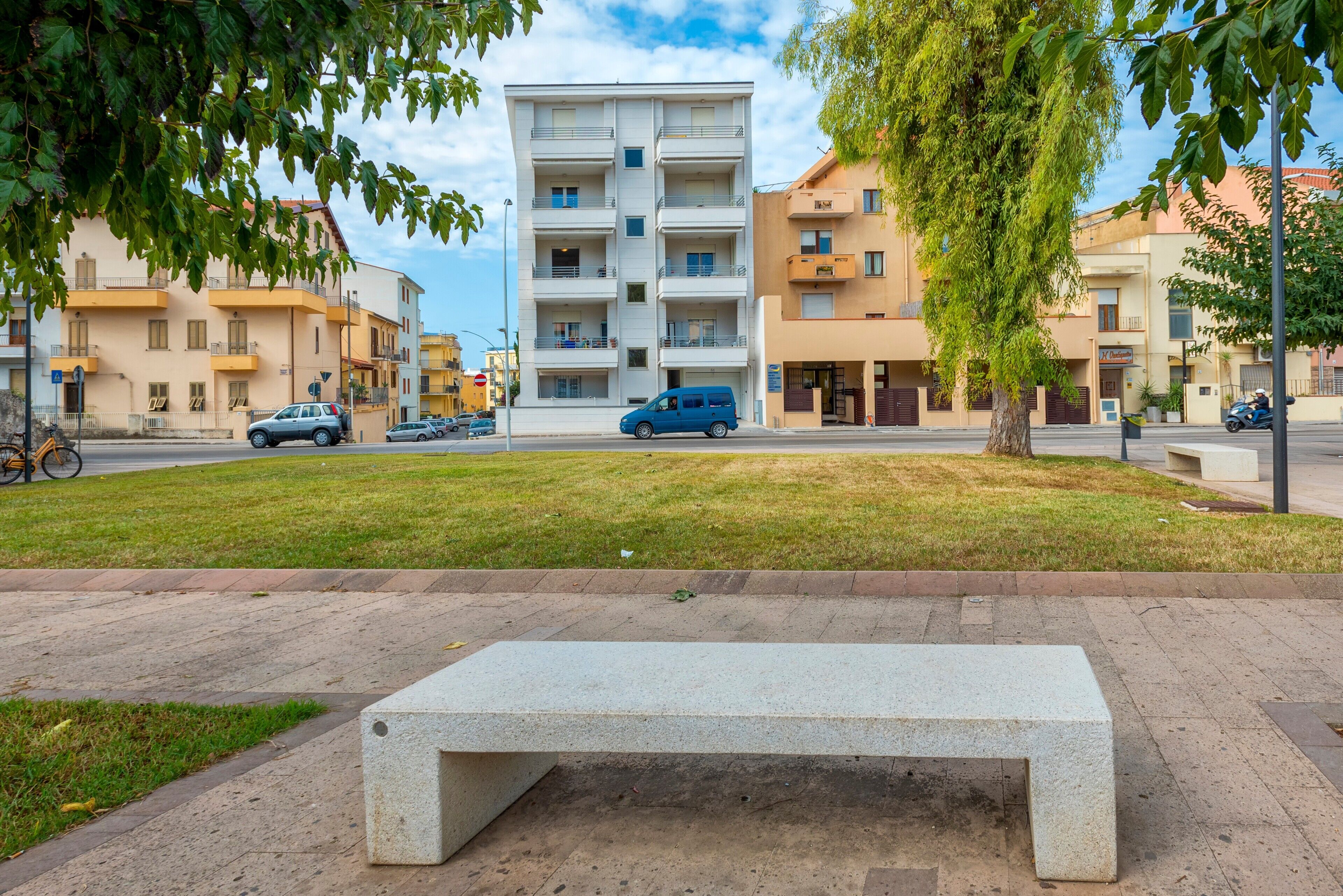 Un banco en una zona arbolada con un edificio al fondo.