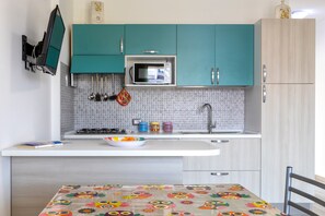 Una cocina con gabinetes color turquesa, un microondas, un fregadero y una mesa con mantel colorido.