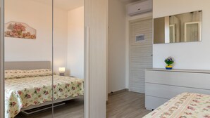 Quarto com cama, mesa de cabeceira, cômoda, espelho e um objeto decorativo na parede.