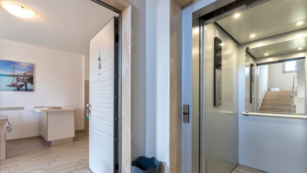 Interior moderno com piso de madeira, uma escrivaninha com cadeira, um vaso azul e uma escada para um andar superior.