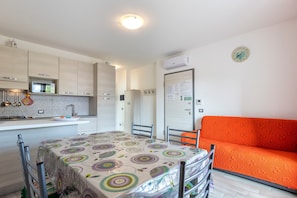 A kitchen with a dining table, chairs, and an orange sofa.