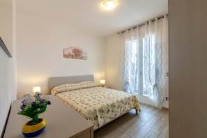 A bedroom with a bed, bedside lamps, a nightstand, a vase with flowers, and a window with curtains.